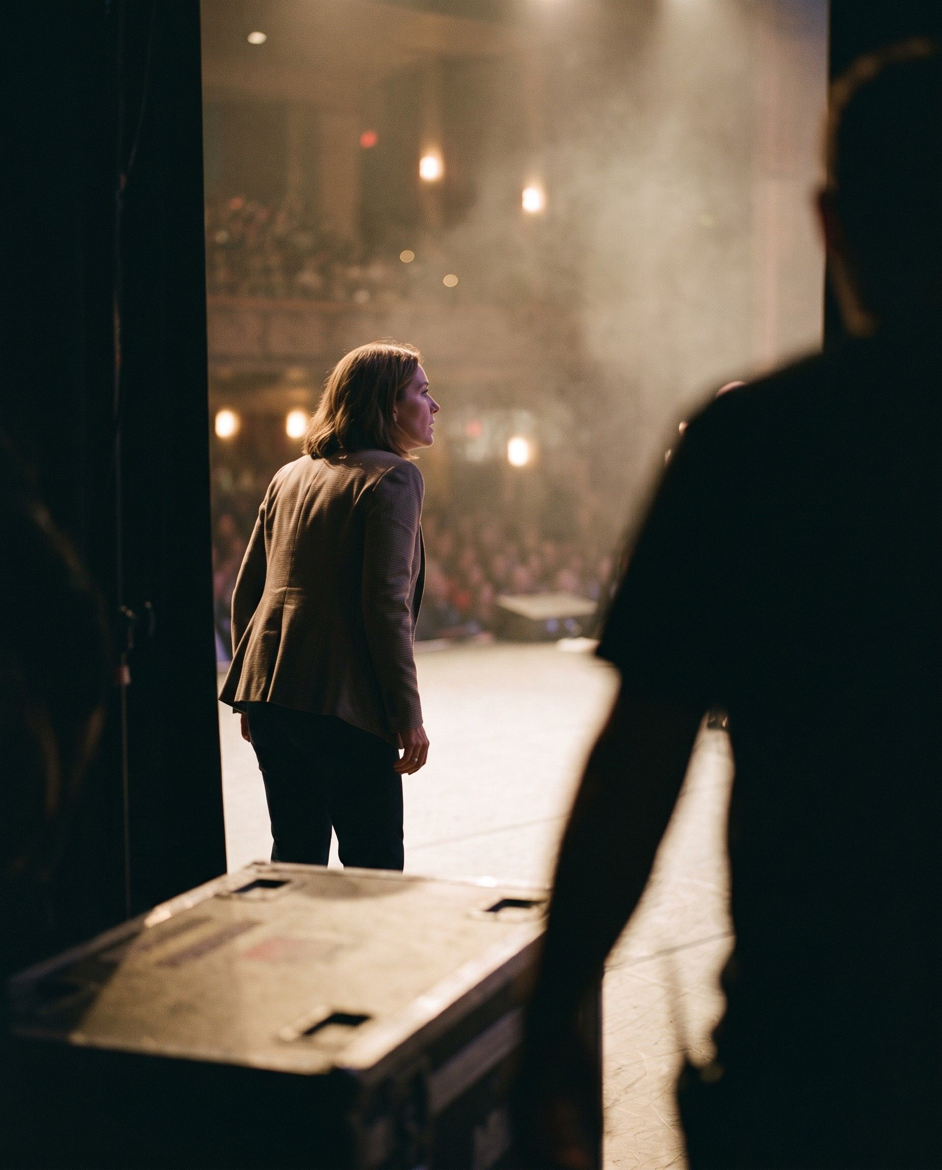 A speaker waiting in the wings of a lit conference stage